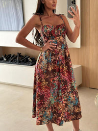 Woman wearing a colorful floral dress in a room with wooden walls and a white cabinet.