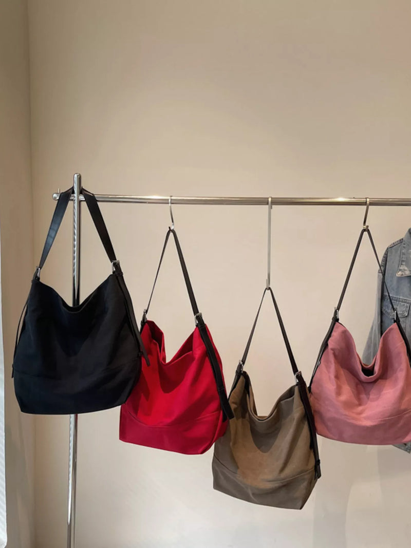 Four handbags in black, red, brown, and pink hanging on a rack against a neutral background.