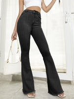 Person wearing black flared jeans with a white top and bag indoors.