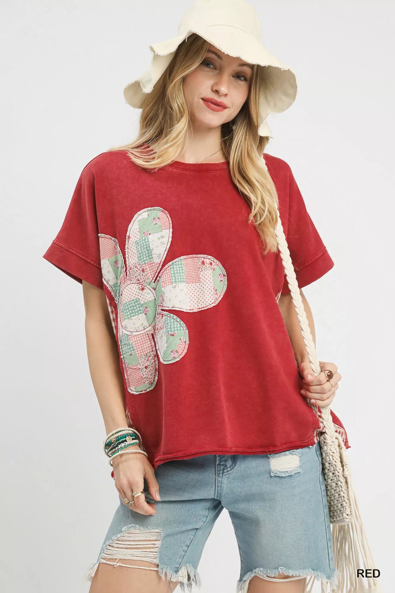 Woman wearing a red t-shirt with a floral design, denim shorts, and a straw hat on a white background.