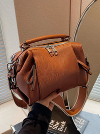 Brown leather handbag held by a person with a neutral background