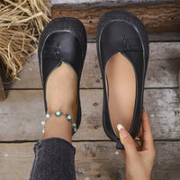 Black flat shoes being held on a wooden floor