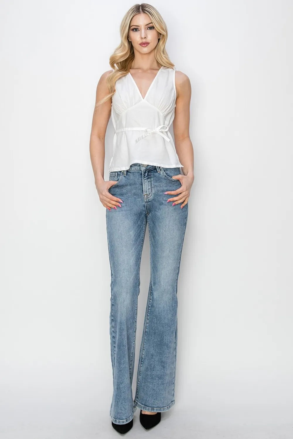 Woman wearing a white sleeveless top and blue jeans on a white background