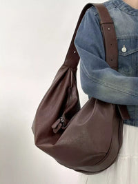 Brown leather bag carried by a person wearing a blue denim jacket on a light background