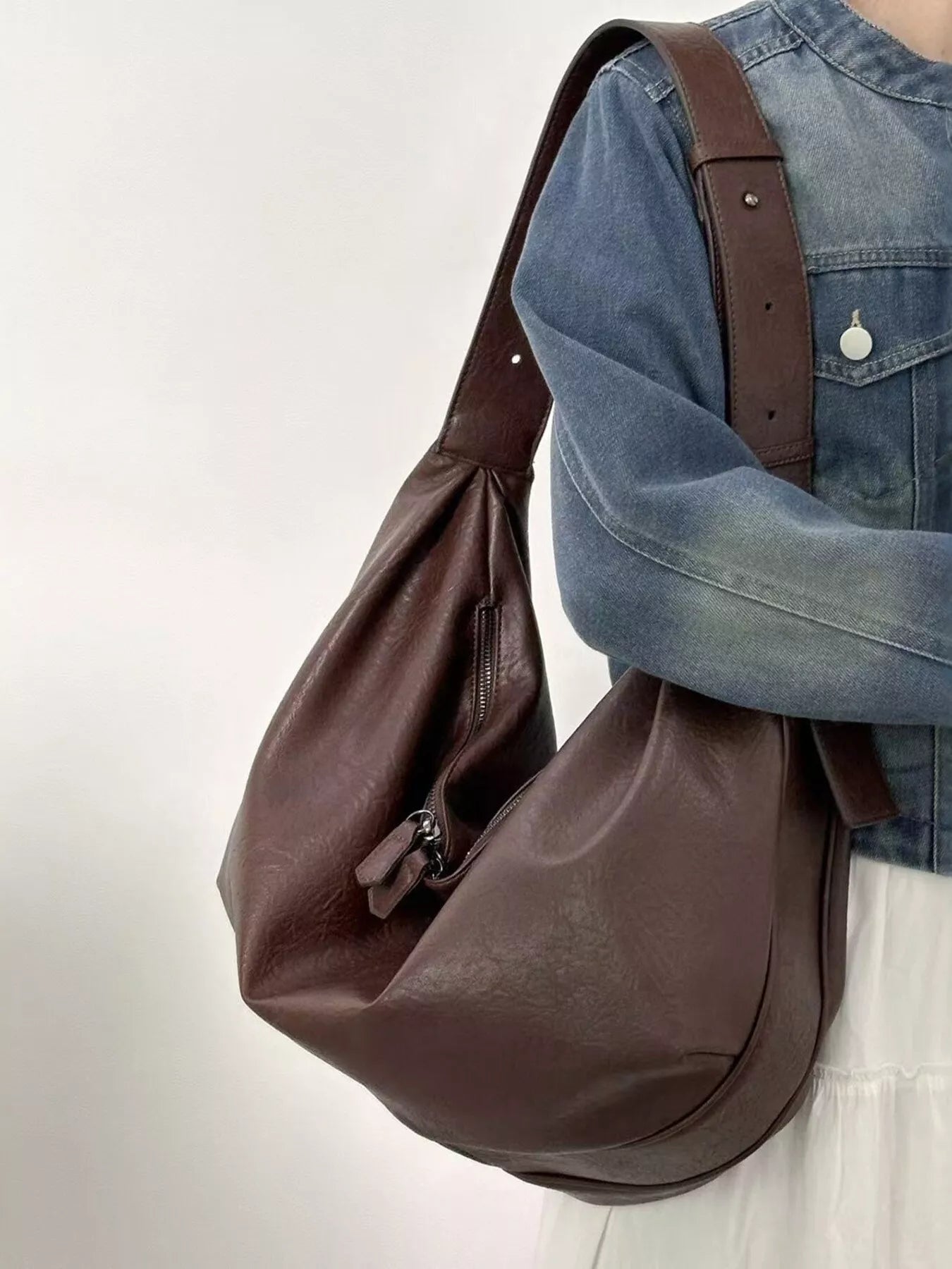 Brown leather bag carried by a person wearing a blue denim jacket on a light background
