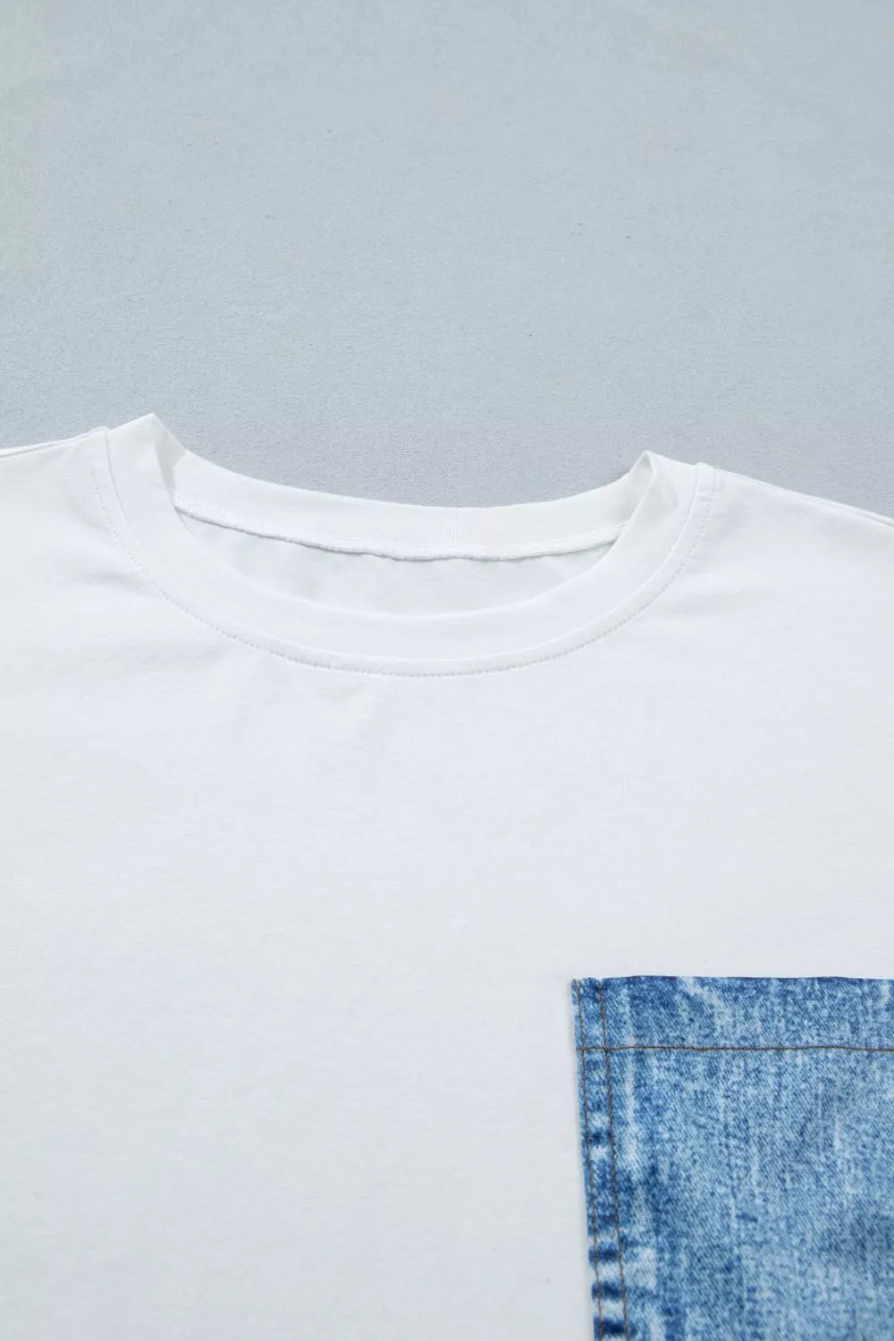 White t-shirt with a blue denim pocket on a gray background