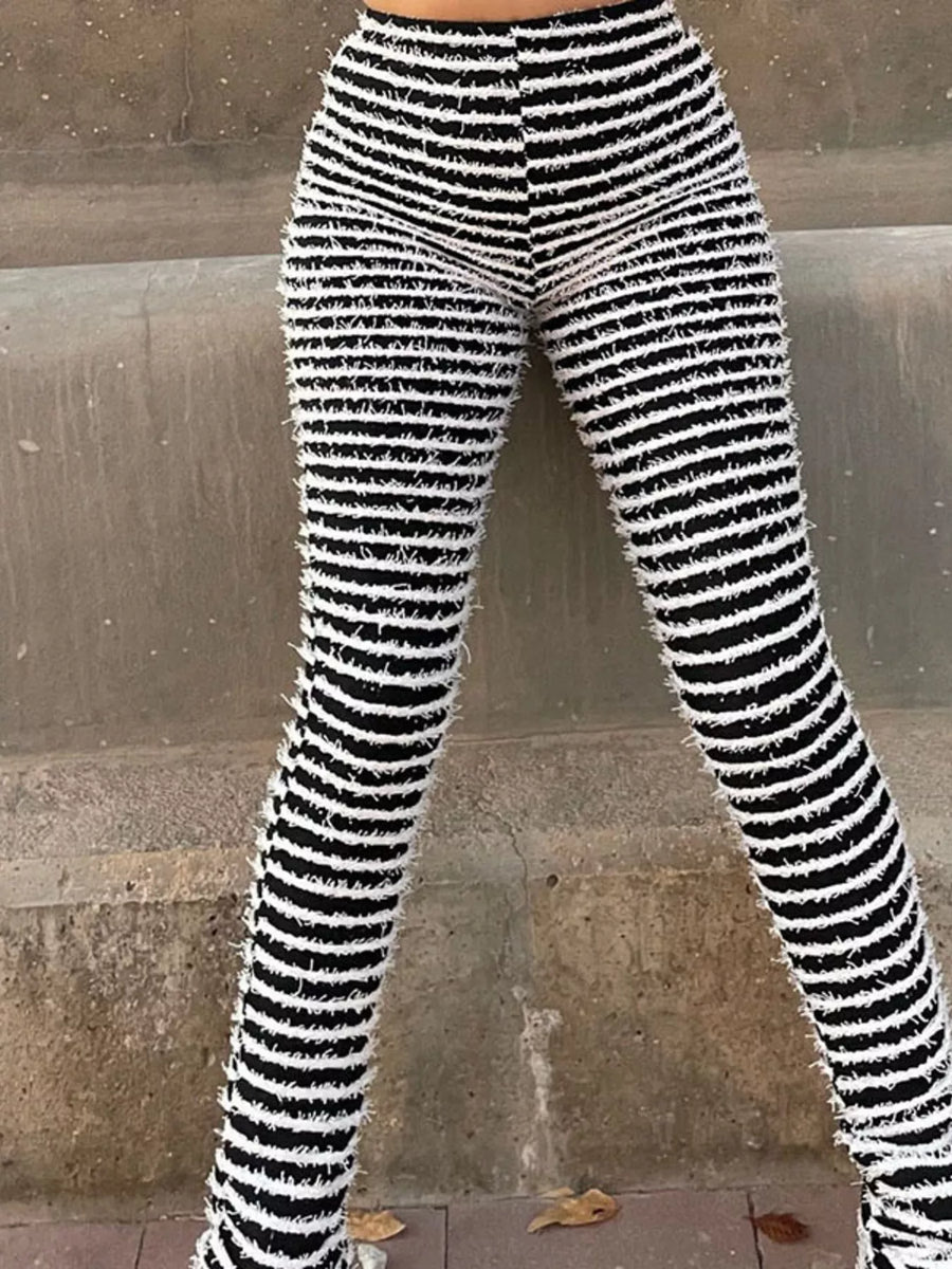 Black and white horizontally striped fuzzy knit flare leggings worn by a model standing against a concrete wall.