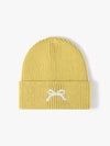 Yellow knit beanie with a white bow design on a light gray background