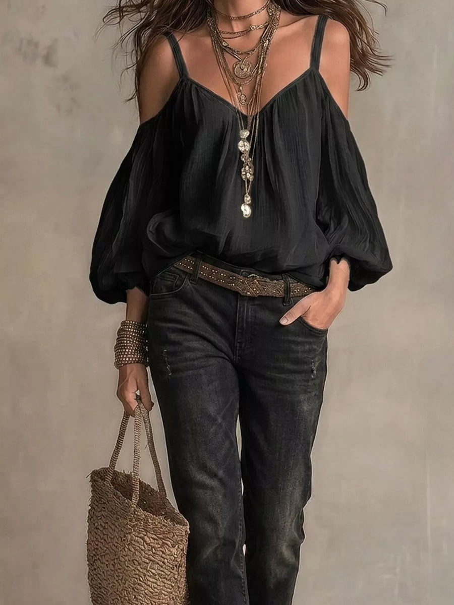 Woman wearing a black blouse and dark jeans, holding a woven bag against a neutral background
