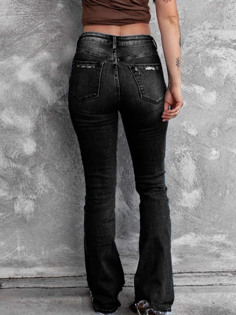 Person wearing black flared jeans against a textured gray wall.