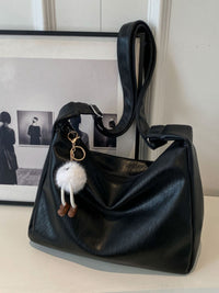 Black handbag with a fluffy keychain on a white surface