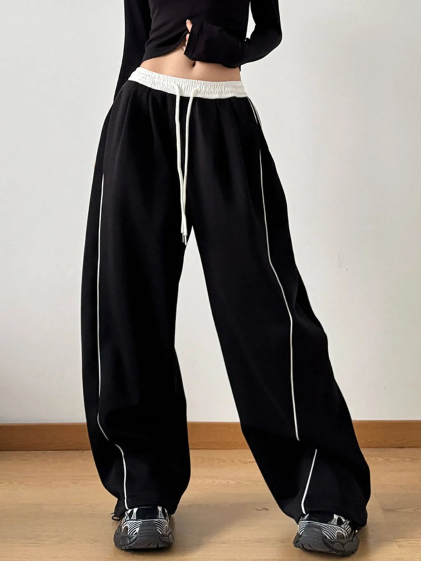 Black wide-leg pants with white drawstring and piping on a plain background