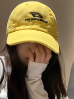 Person wearing a yellow cap with a brand logo on a neutral background