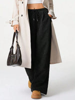 Person wearing a long beige coat, black pants, and brown shoes on a white background