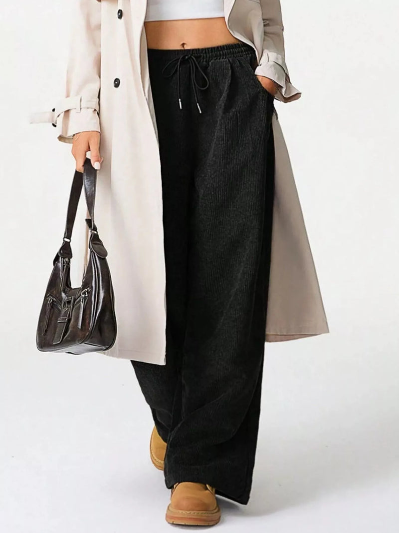 Person wearing a long beige coat, black pants, and brown shoes on a white background