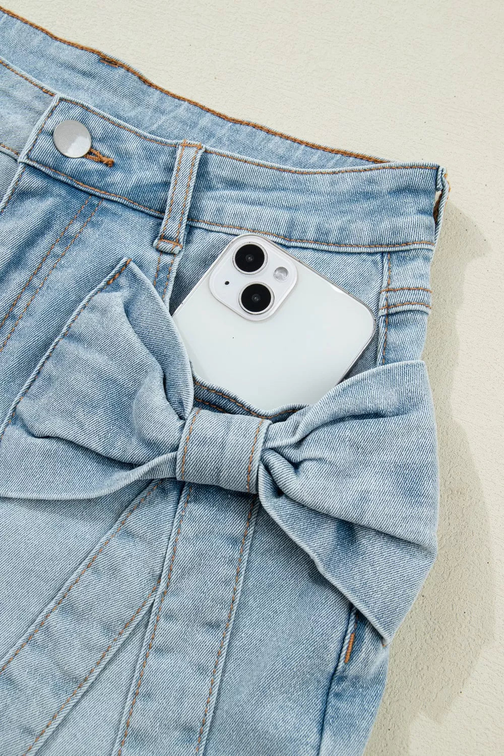 White phone in a blue denim pocket with a bow detail