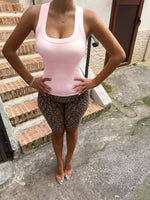 Person wearing a pink tank top and leopard print shorts standing on a concrete path.