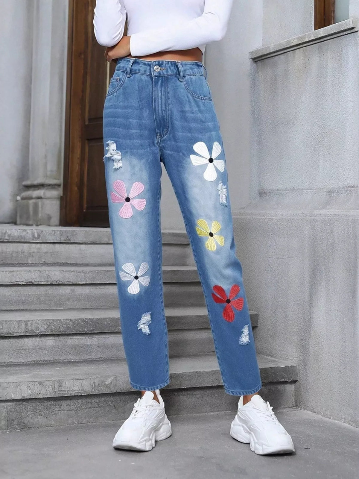 Person wearing blue jeans with colorful floral patches on a stone staircase.