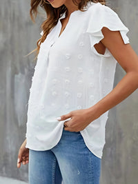 Woman wearing a white blouse with ruffled sleeves and blue jeans against a gray wall.
