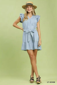 Woman wearing a light denim dress with ruffled sleeves and a belt on a green background