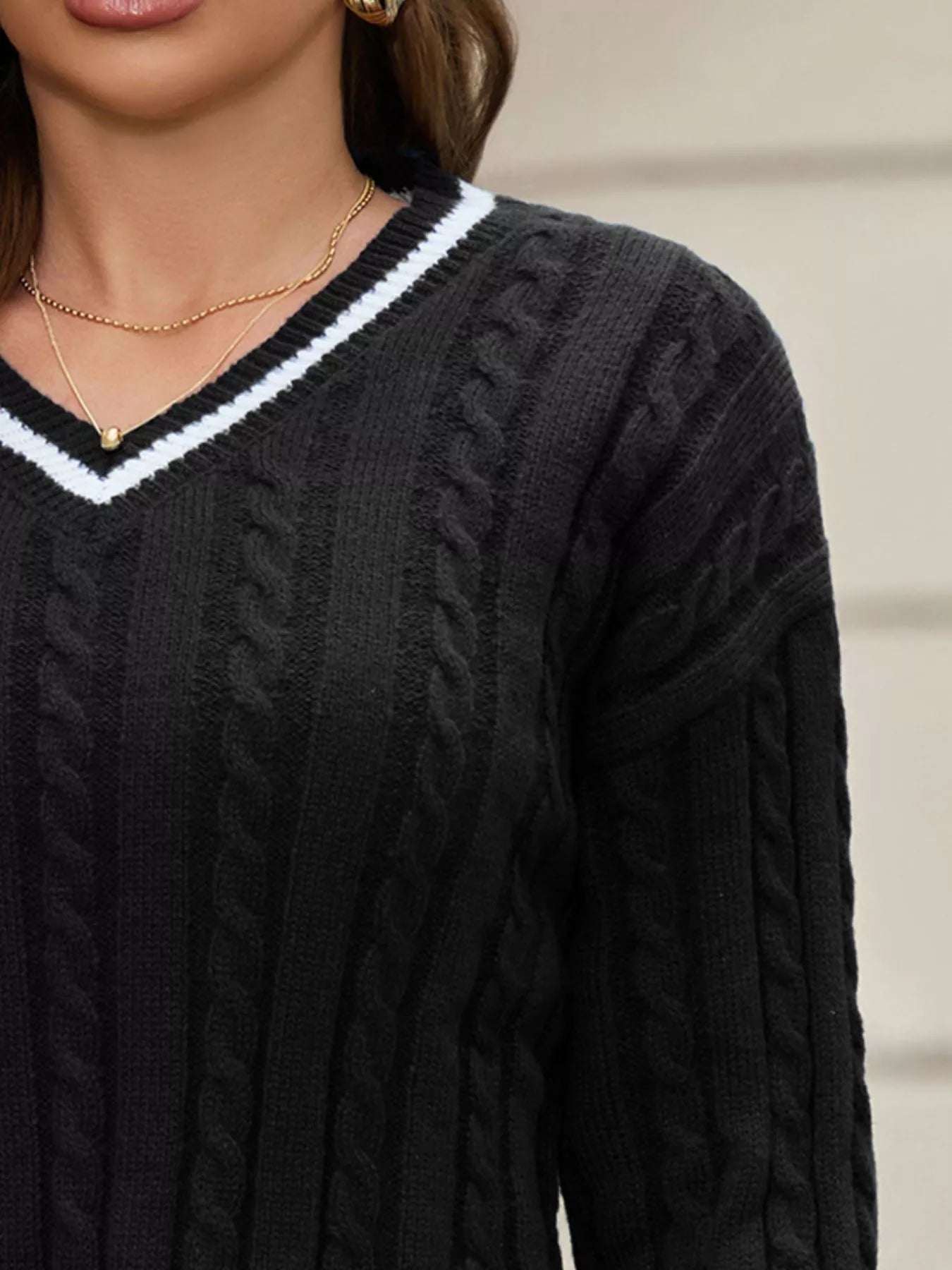 Black cable knit sweater with white trim worn by a person.