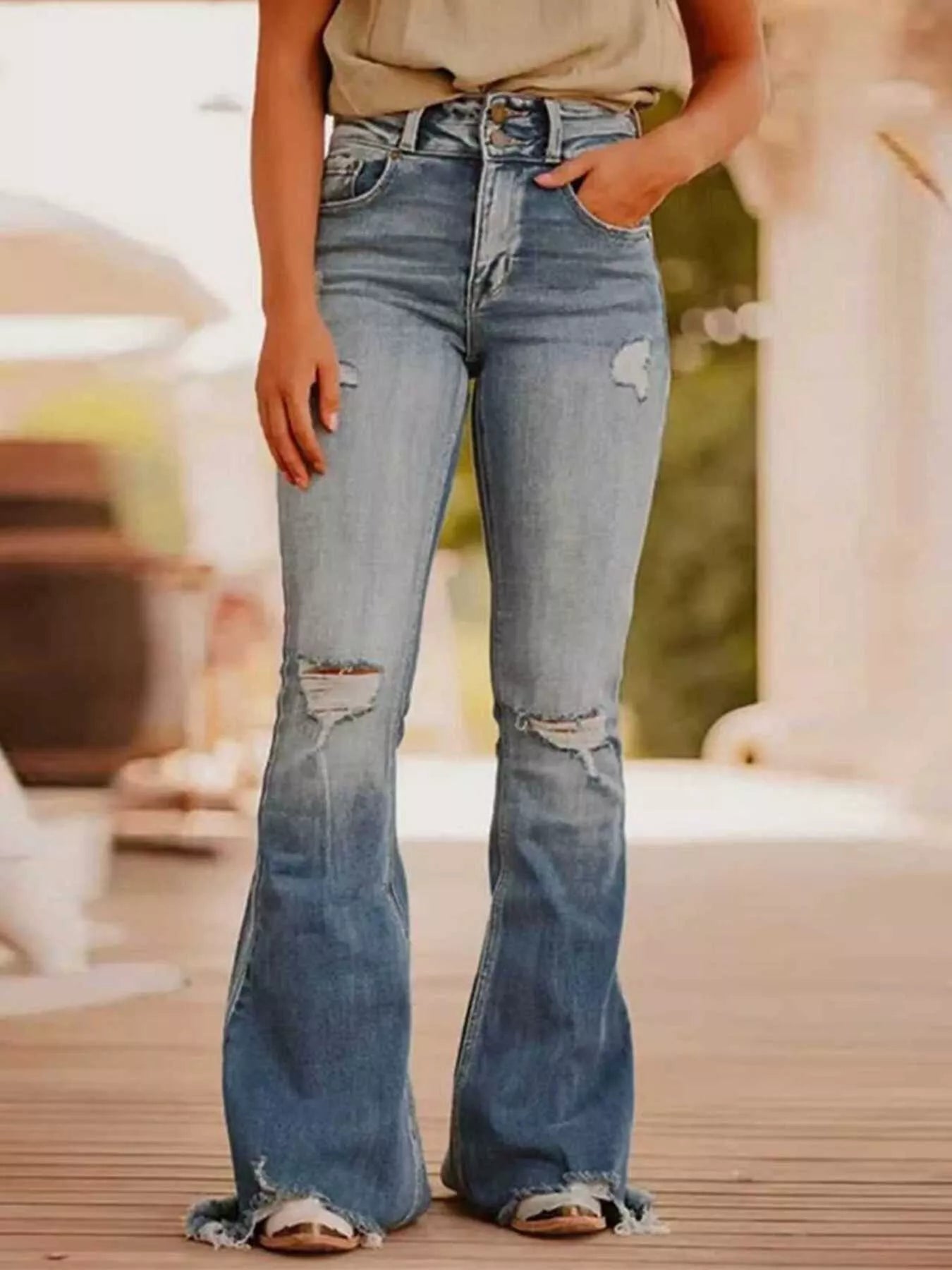 Person wearing distressed blue jeans standing outdoors with a blurred background