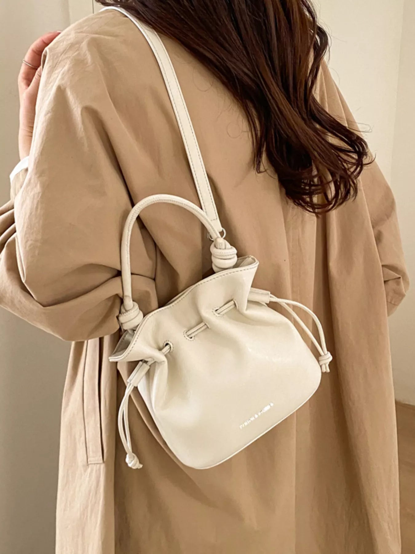 Person wearing a beige coat with a white drawstring bag over their shoulder.