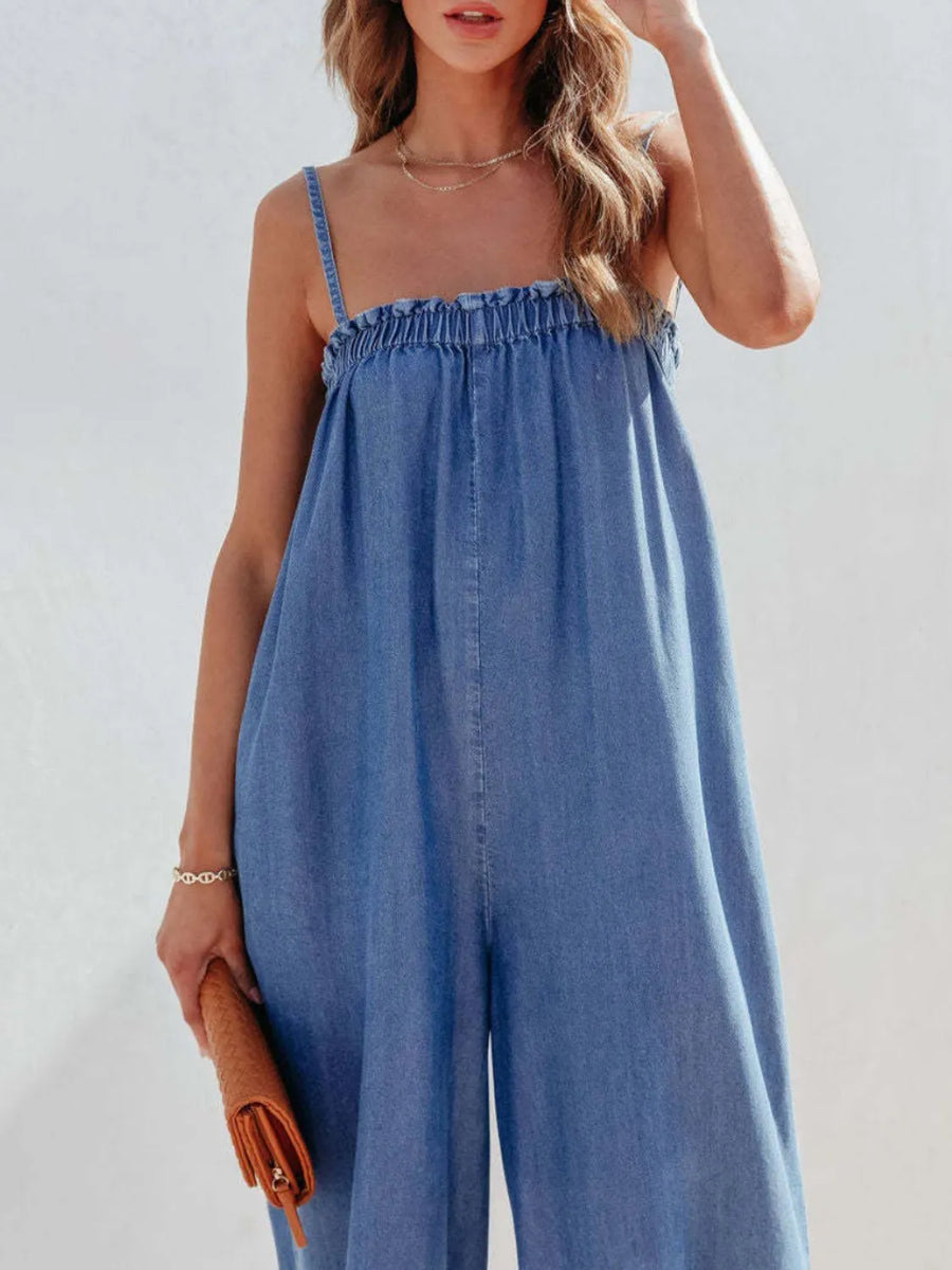 Woman wearing a blue denim jumpsuit against a plain background