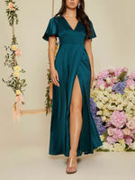 Woman wearing a teal dress with a slit in front, standing against a floral background.