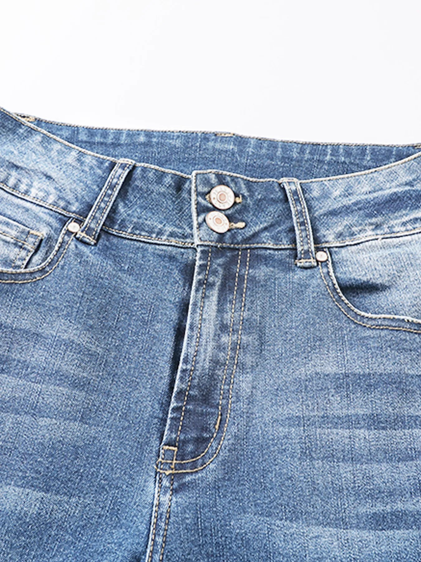 Close-up of a blue denim jeans waistband with buttons and stitching details.