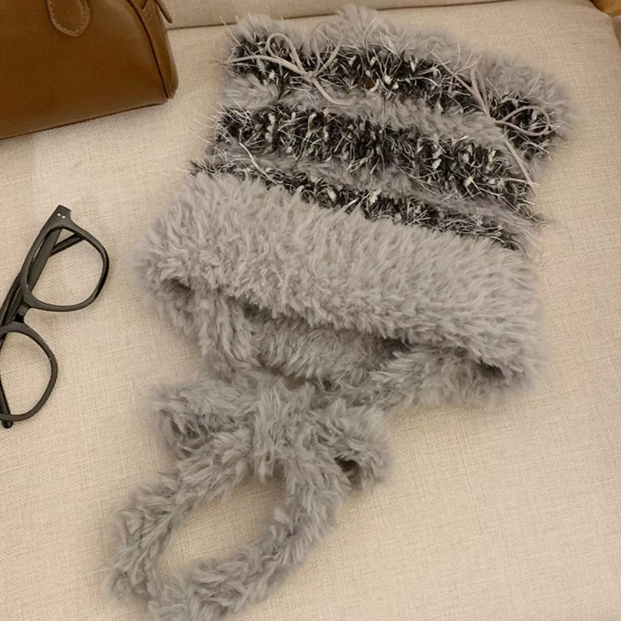 Gray fuzzy scarf on a beige surface with a brown bag and black glasses nearby