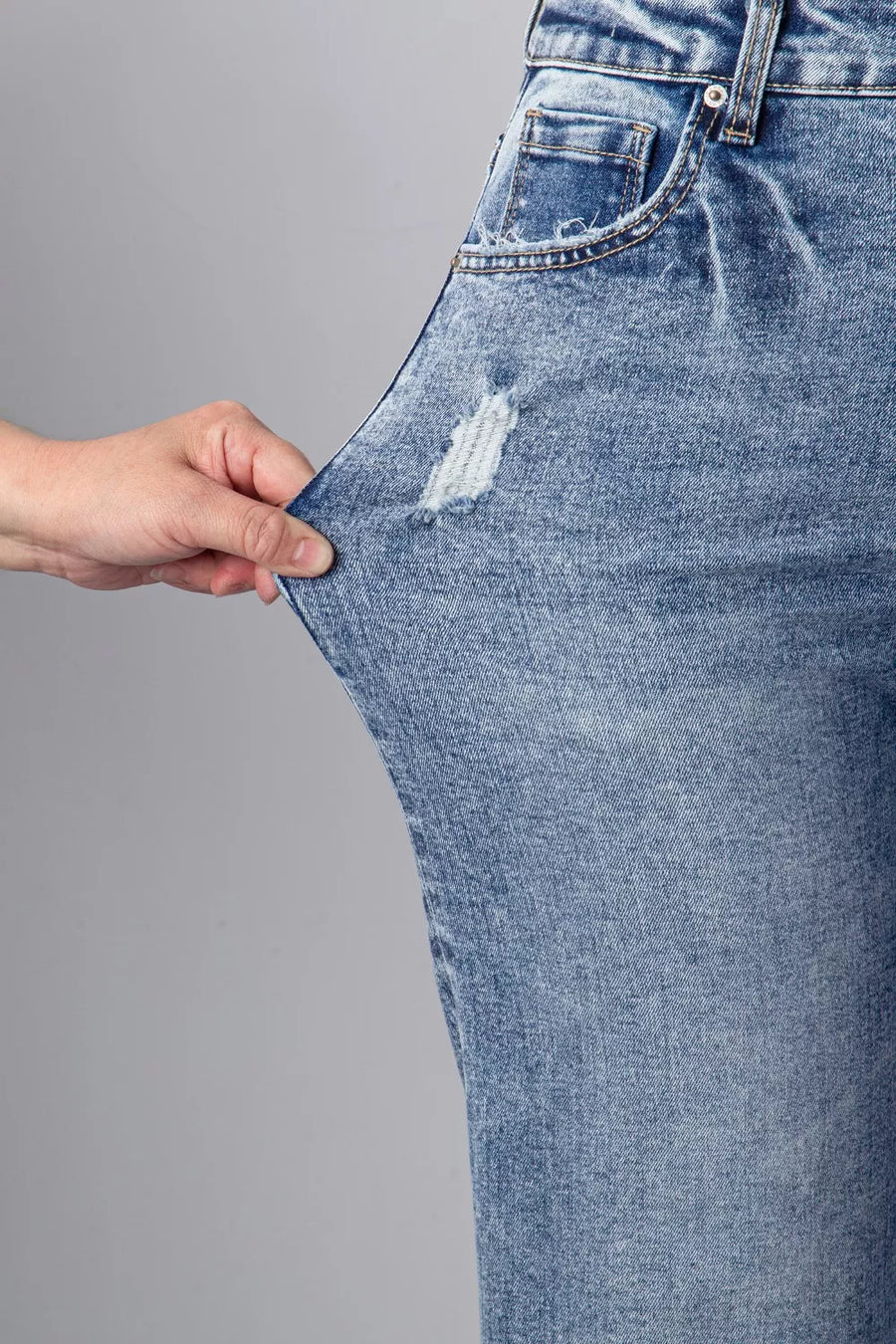 Close-up of a person holding a blue denim jeans leg with a gray background
