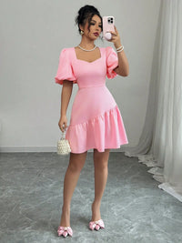 Woman in a pink dress taking a mirror selfie in a room with gray flooring and white walls.