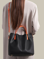 Person wearing a black leather handbag with orange straps on a neutral background