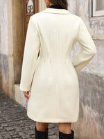 Person wearing a white coat walking on a cobblestone street.