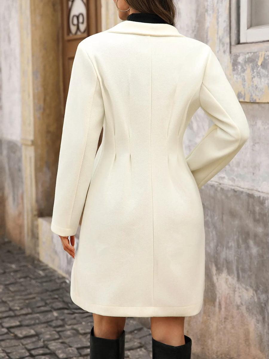 Person wearing a white coat walking on a cobblestone street.