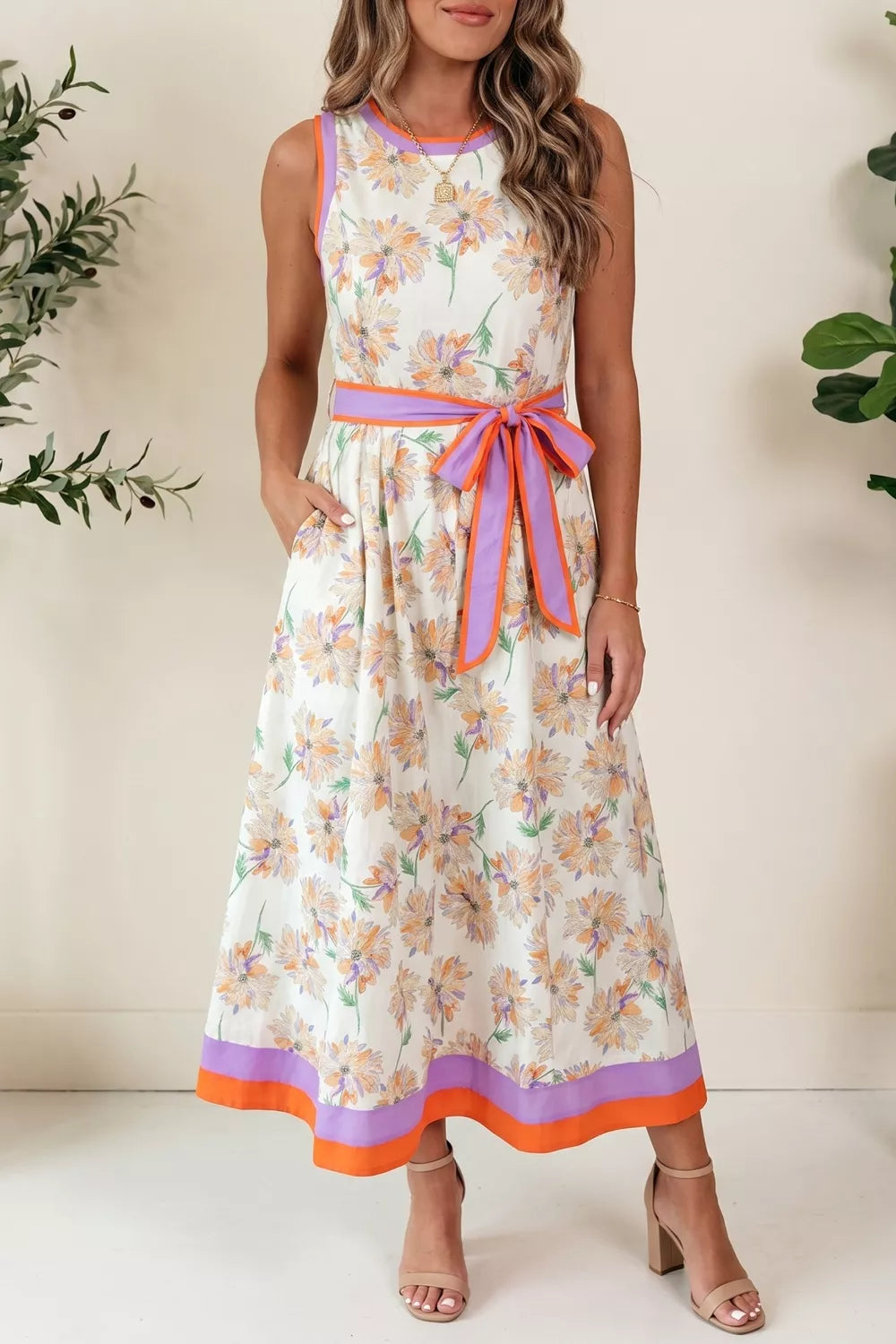 Woman wearing a floral dress with a belt, standing against a neutral background.