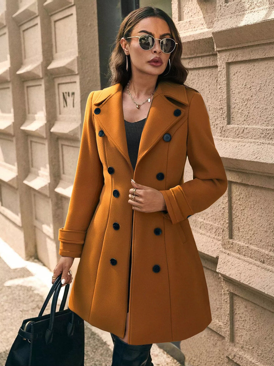 Woman wearing a mustard yellow coat with black buttons against a textured wall.