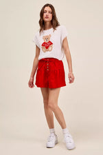 Woman wearing a white t-shirt with a teddy bear graphic and red shorts on a beige background