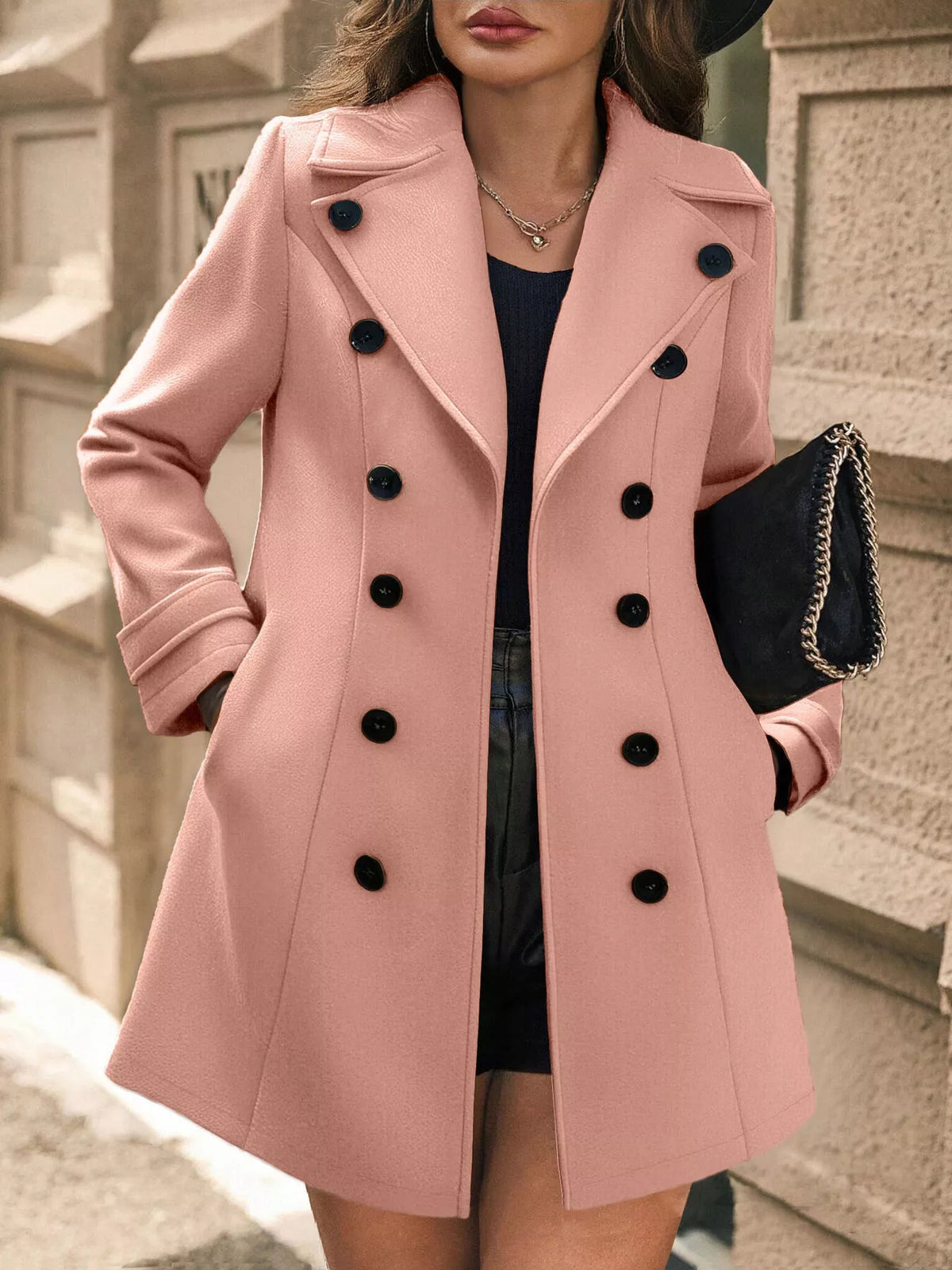 Woman wearing a pink coat with black buttons outdoors.