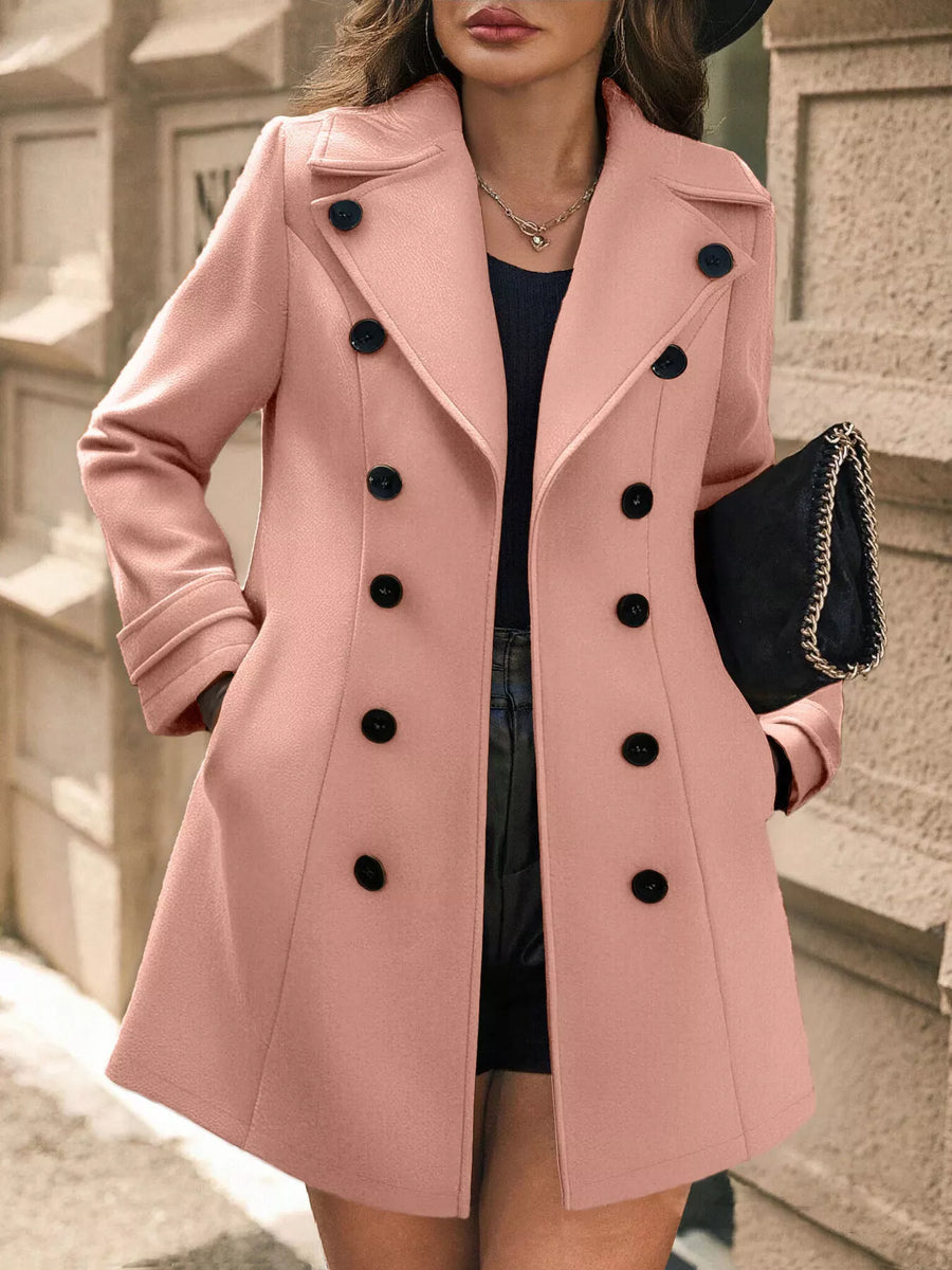 Woman wearing a pink coat with black buttons outdoors.