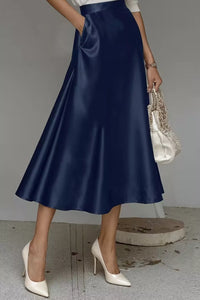 Person wearing a navy satin skirt with white high-heeled shoes and a beaded clutch.