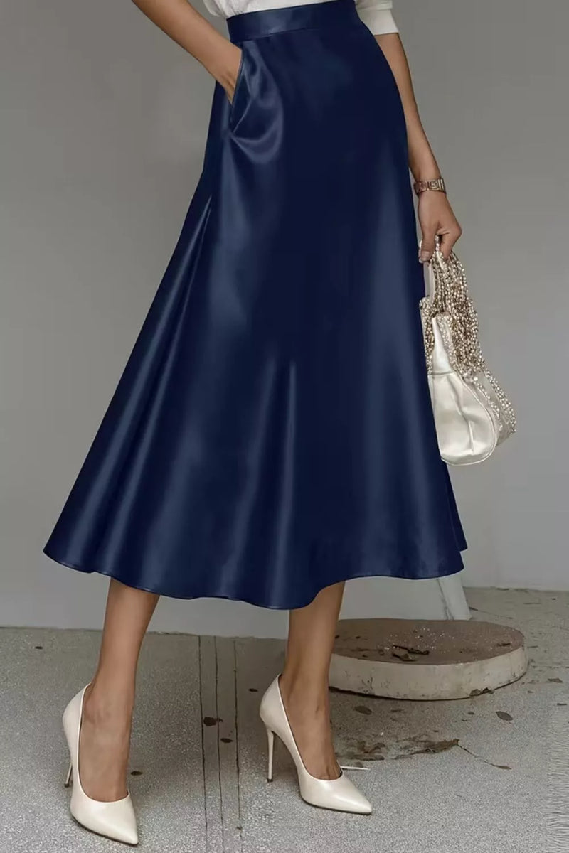 Person wearing a navy satin skirt with white high-heeled shoes and a beaded clutch.