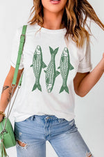 Person wearing a white t-shirt with green fish graphics, holding a green handbag.