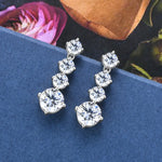 Silver earrings with clear gemstones on a blue surface with flowers in the background