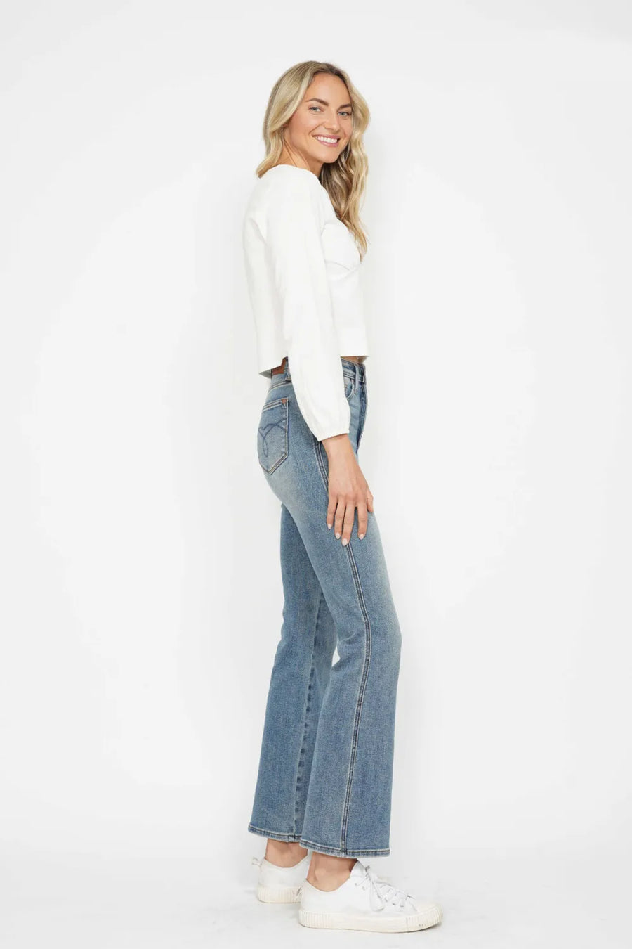 Woman wearing a white long-sleeve top and blue jeans on a white background