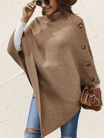 Woman wearing a brown poncho with buttons, holding a brown handbag against a light background