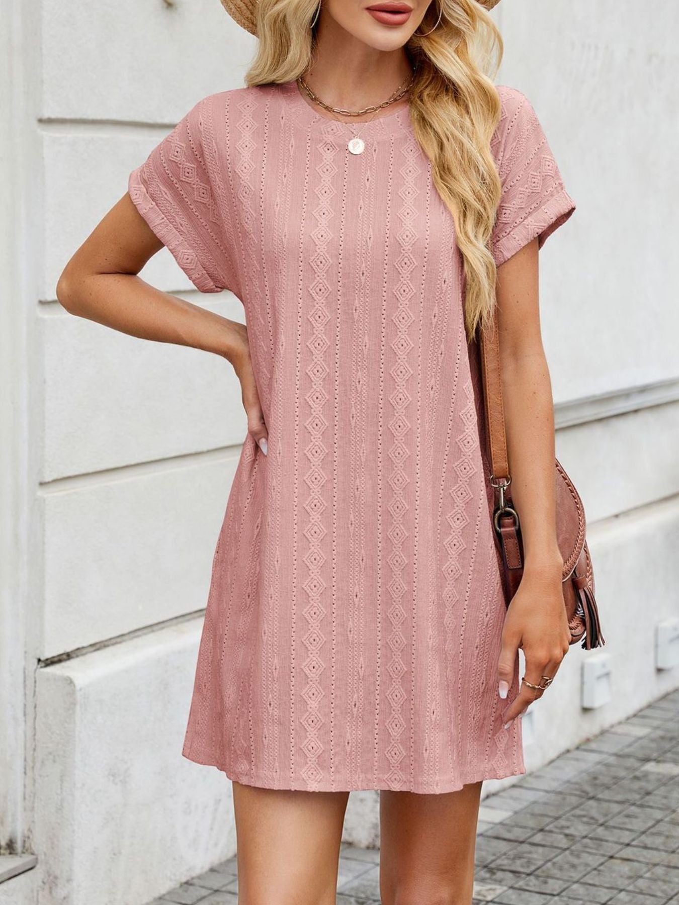 Woman wearing a pink lace dress standing against a white wall.
