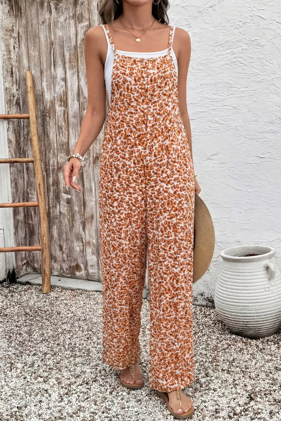 Person wearing a floral jumpsuit standing against a rustic wooden wall.