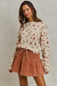 Woman wearing a floral sweater and brown skirt against a plain background